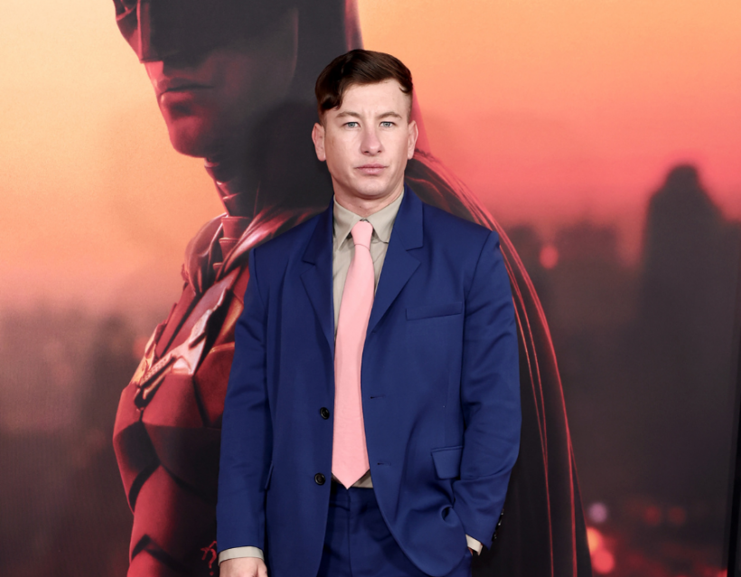Barry Keoghan at The Batman premiere standing in front of robert pattinson as batman poster