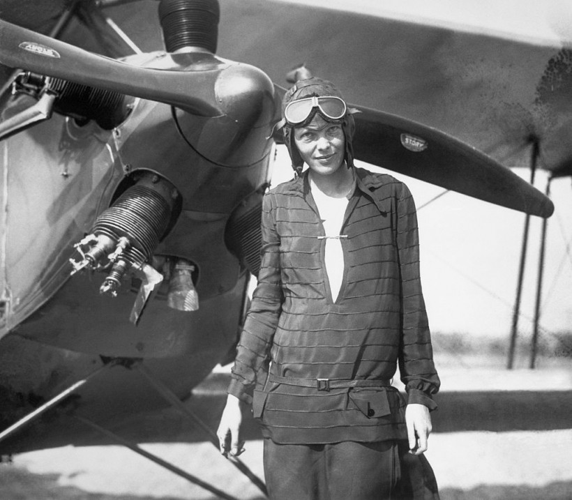 Amelia Earhart stands in front of her airplane.