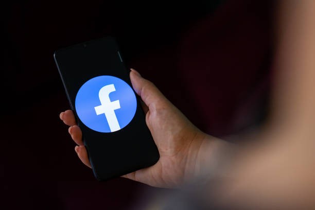A hand holding a mobile phone with the logo of Facebook on its screen. 