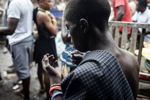 A young man stares at his hand as he smokes Kush inside a drug den at the Kington landfill site in Freetown on June 21, 2023. In recent years Kush, a mix of various chemicals and plants that mimic the natural properties found in cannabis, according to the National Drug Agency, is increasingly being used by youth in Sierra Leone. At only 25 US cents a dose, the drug is addicting users. 