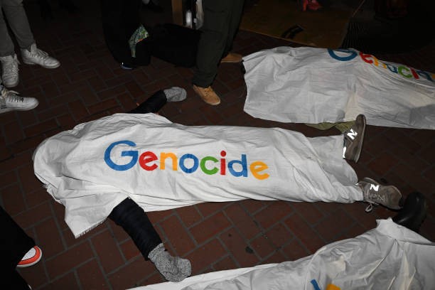 SAN FRANCISCO, CALIFORNIA - DECEMBER 14: About a dozen demonstrators lay on the ground draped in white sheets with a mock version of the Google logo spelling out the word 'genocide', as hundreds of protestors including Google workers are gathered in front of Google's San Francisco offices and shut down traffic at One Market Street block on Thursday evening, demanding an end to its work with the Israeli government, and to protest Israeli attacks on Gaza, in San Francisco, California, United States on December 14, 2023. 